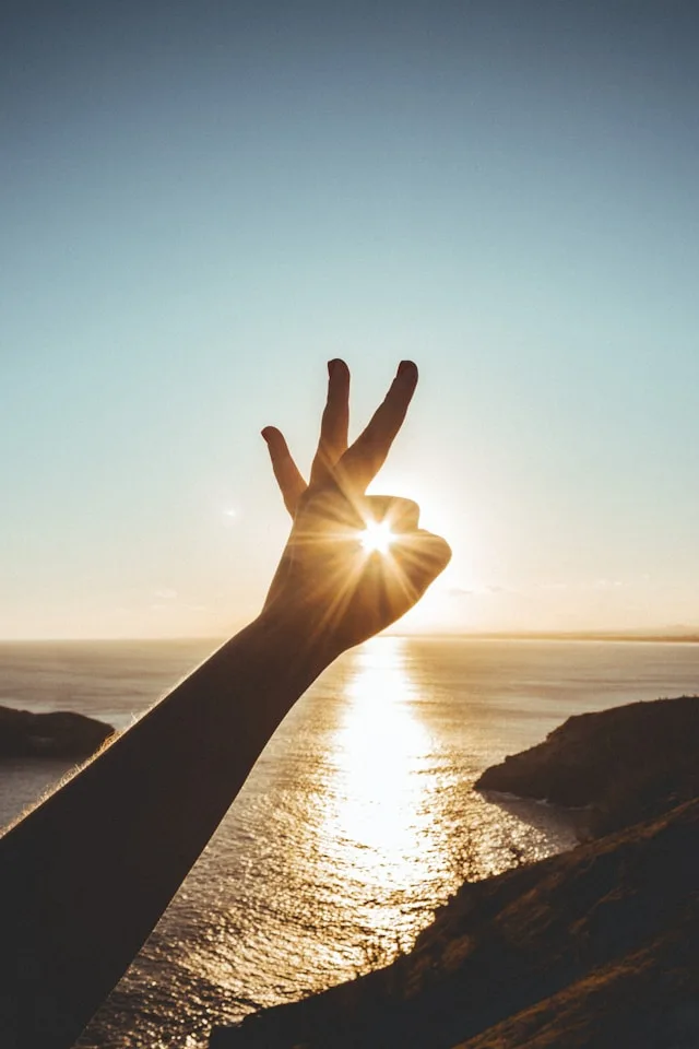 Hand making a victory sign at sunset